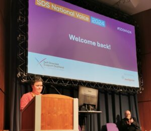 Woman standing behind lectern in front of screen which reads 'SDS National Voice 2024 Welcome back!'